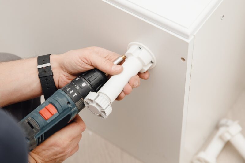 momak koristi bušilicu i postavlja nogicu za kuhinjski nameštaj