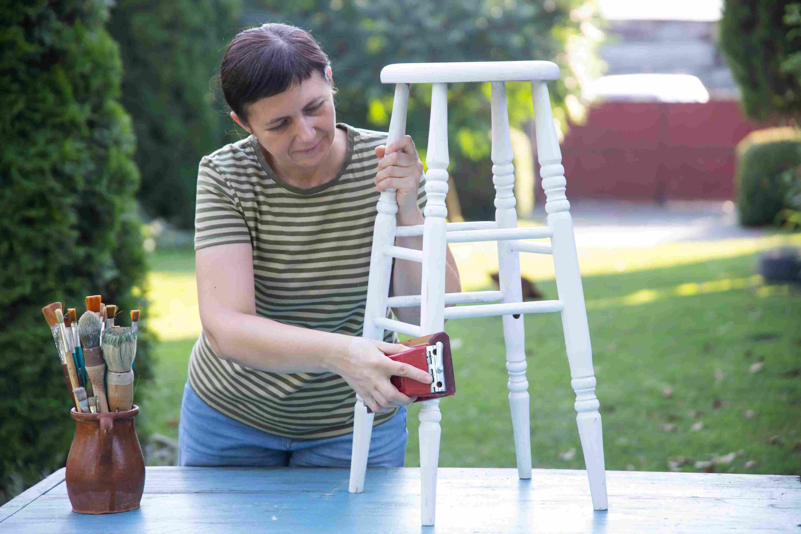 Žena šmirgla drvenu stolicu tokom restauracije u dvorištu